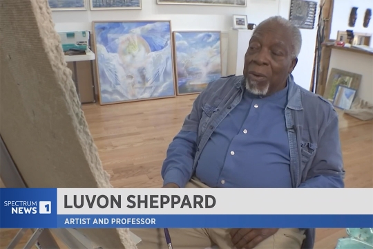 a man in a blue shirt sits in front of an artist canvas.