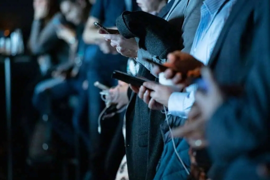 a crowd of adults in suits all look at their phones