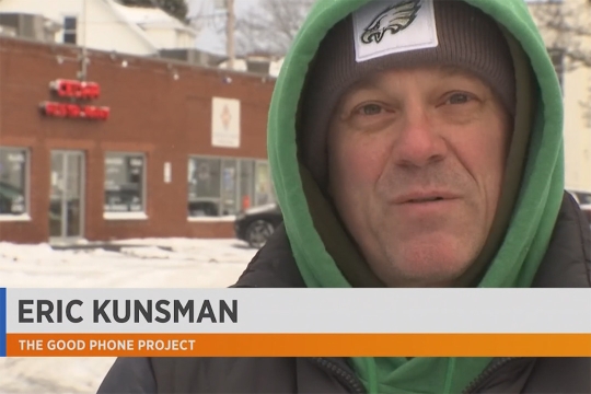 A still from the news video featuring Eric Kunsman. Eric is speaking to the camera, wearing a green hoodie and Eagles beanie. A graphic along the bottom of the image reads Eric Kunsman, The Good Phone Project.