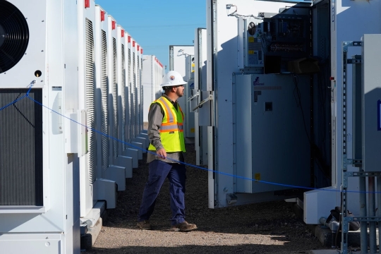 a man in contruction apparel walks through large battery storage systems