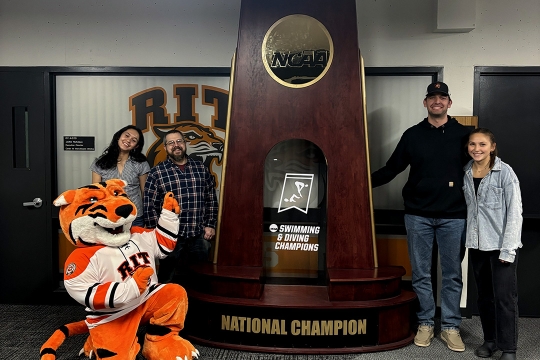Students and a tiger mascot pose by a large trophy.
