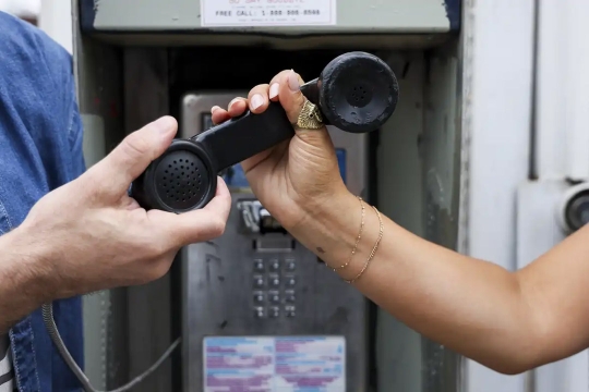 two hands hold the reciever of a payphone.