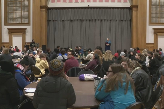 groups of people sit at tables looking at a stage.