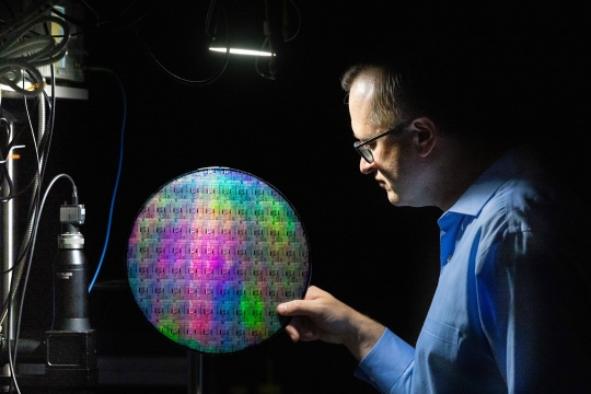 a man in profile holds a quantum photonic wafer against a black background.