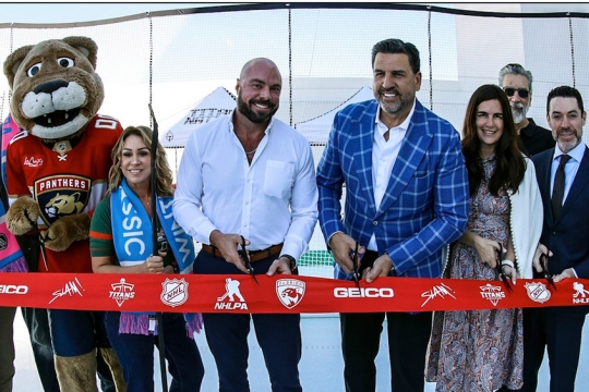 A group of people and costumed mascots prepare to cut a ribbon to open an ice skating rink.