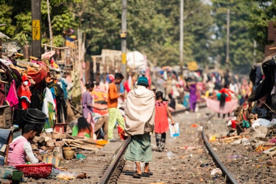 a photo from behind a man walking down a railroad track in an over crowded village in India.