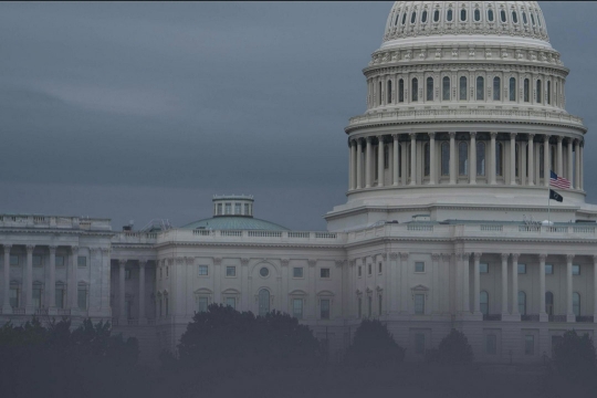 A large white building with a dome, fading behind clouds.