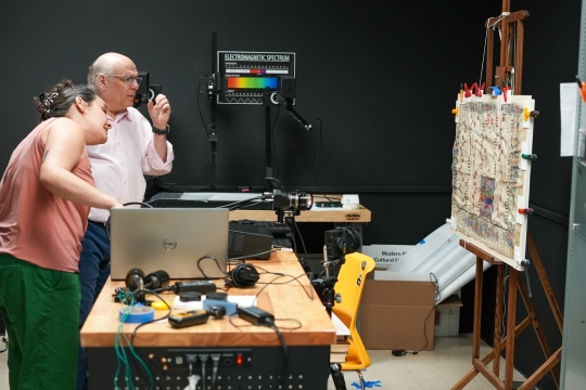 2 individuals using imaging equipment to inspect a piece of artwork