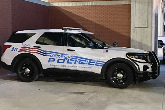 a detroit police S U V is parked in an alley next to a brick building.