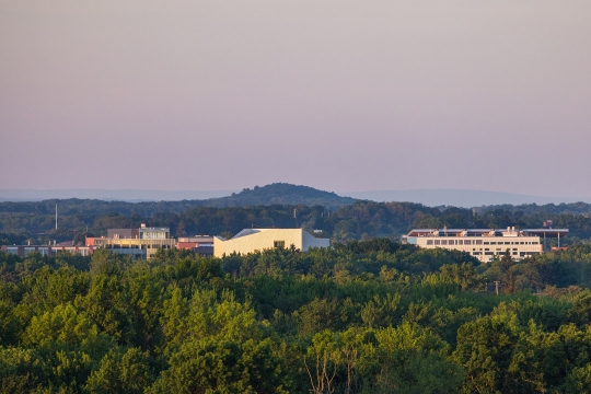 The tops of buildings on the R I T campus appear during sunrise behind trees.