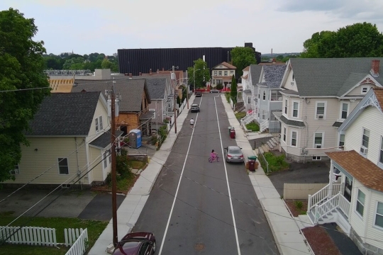 a typical suburban street is shown in an arial view with a large data center looming in the background