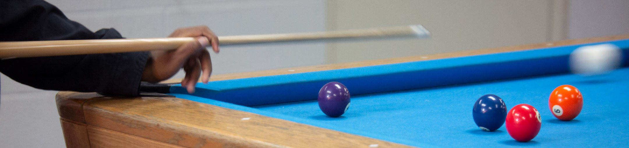 A student's hand playing billiards on a blue pool table.