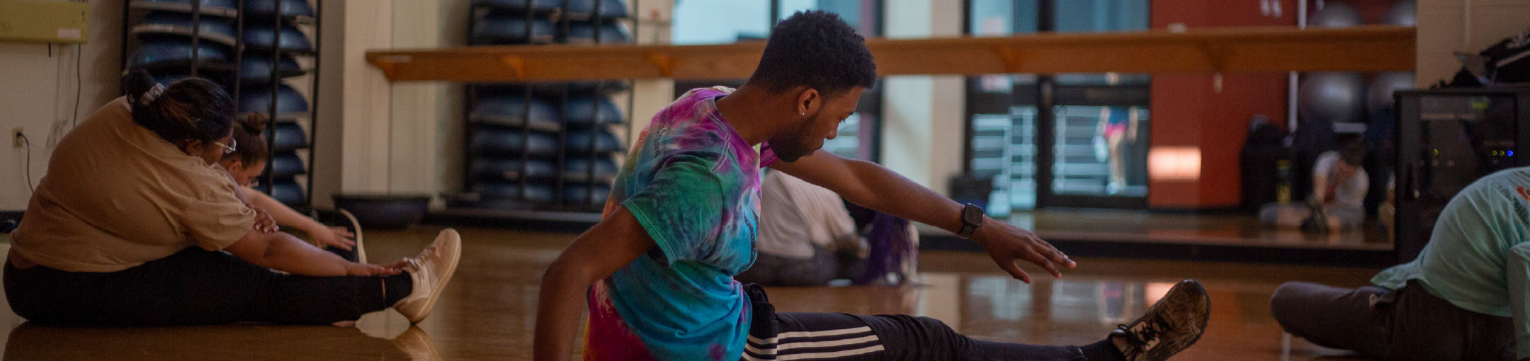 Students sitting on the floor in the dance studio and stretching.