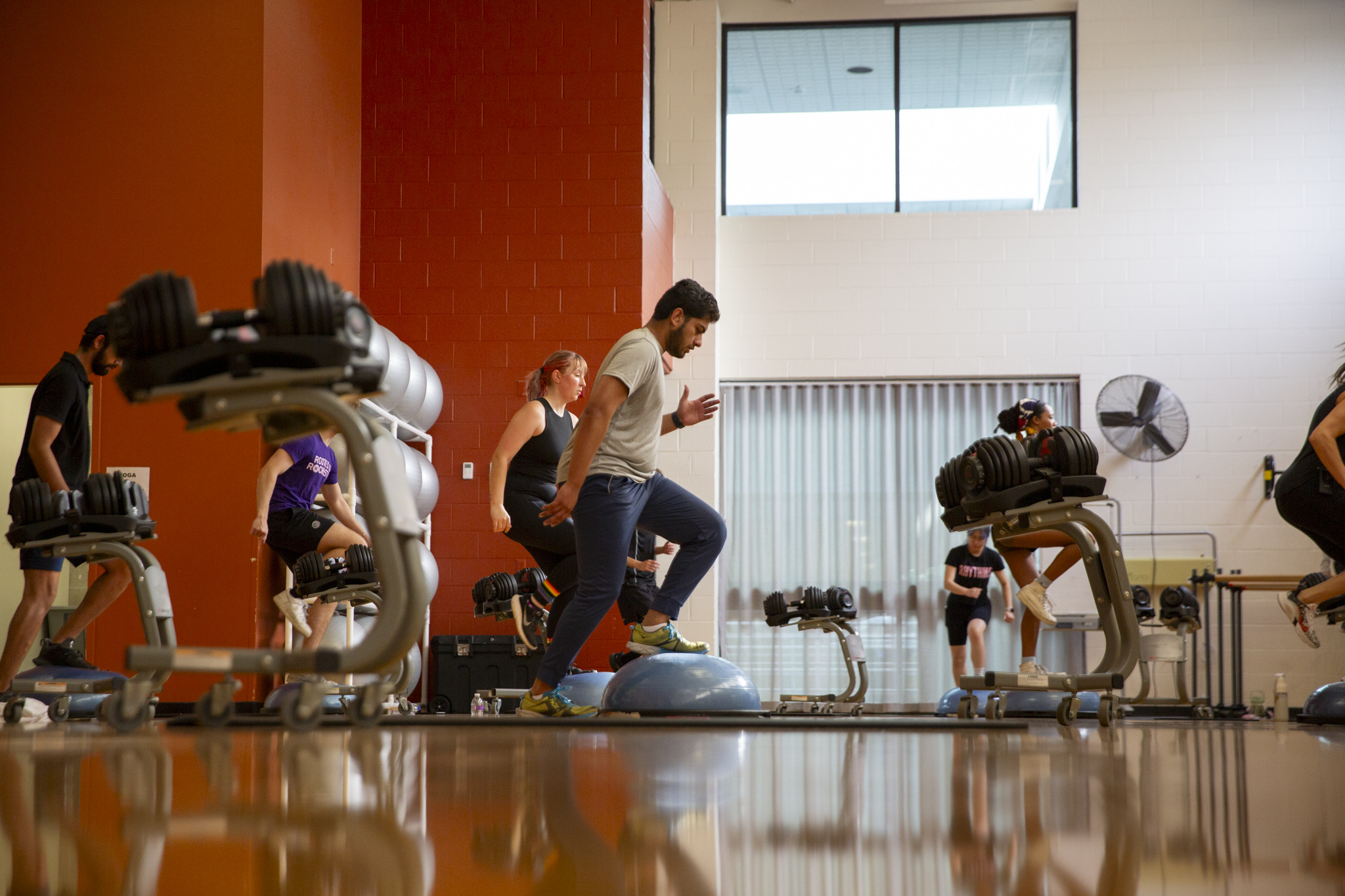 Several people participating in a weight and cardio wellness class in the RIT dance studio gym