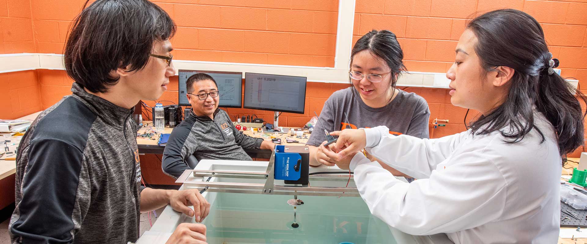 students and a professor adjust lab equipment above a tray of water.