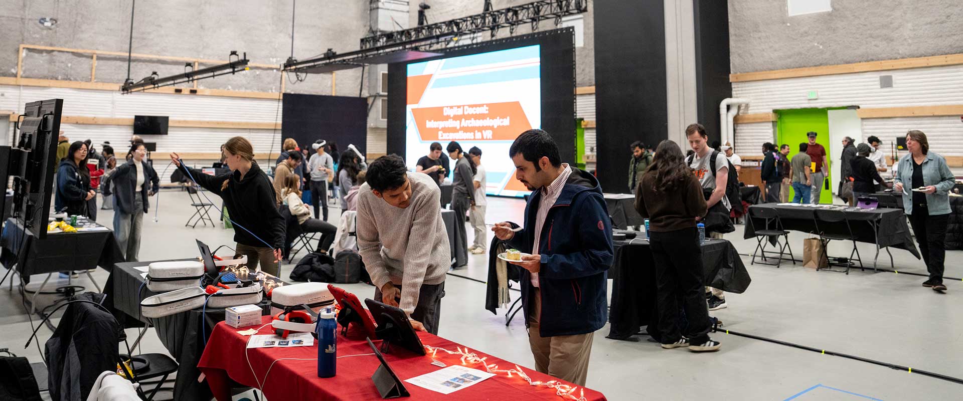 a crowd of people visiting tables at a technology symposium.