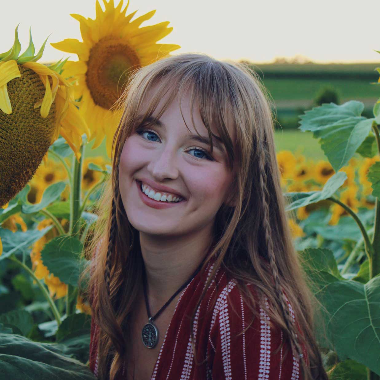 A photo of the 3rd place winner, Isabelle Anderson. She is smiling in a sunflower field at sunset.
