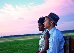 Two people at dusk in a green field. One is wearing a top hat.