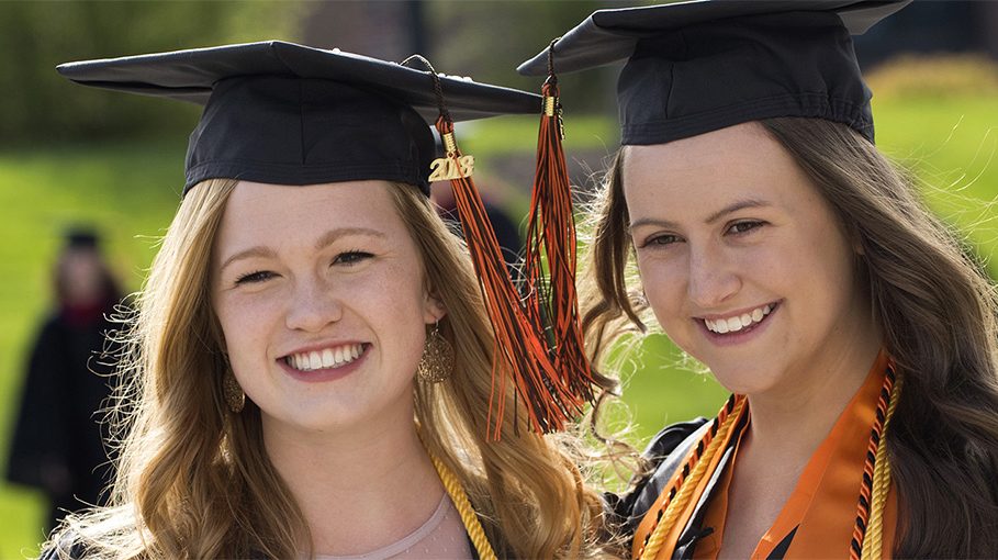 Two graduates posing in their caps and gowns for a photo.