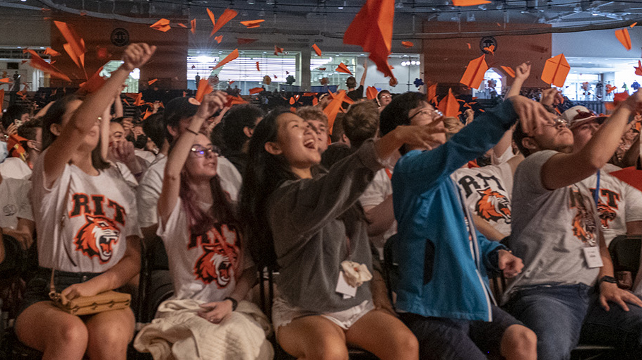 a row of students launching orange paper airplanes into the air