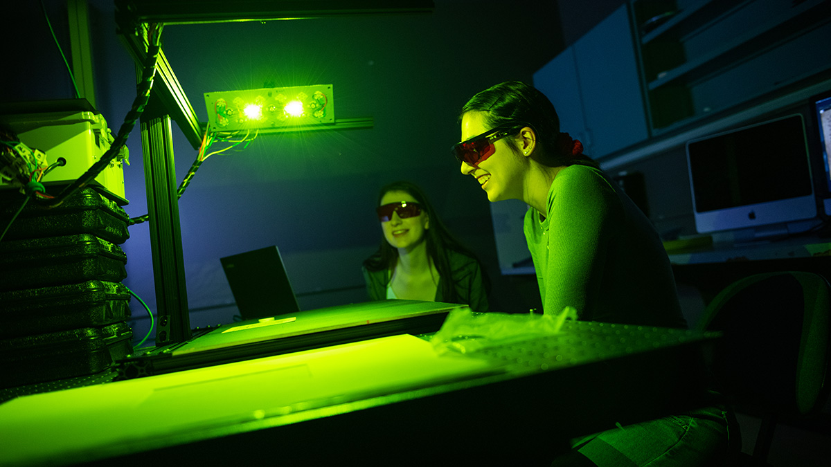 2 people wearing protective glasses, looking at a bright, green light.
