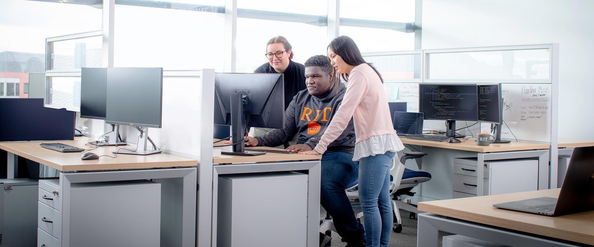 three R I T students looking at a monitor in a computer lab.