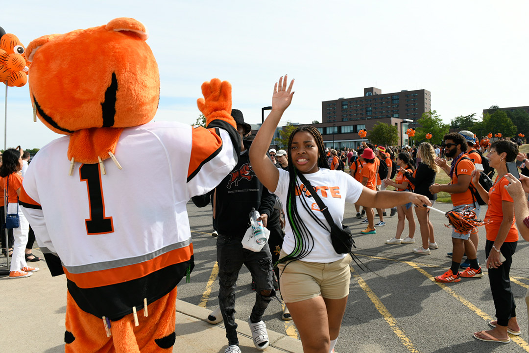Student giving RITchie, the RIT mascot, a high five.