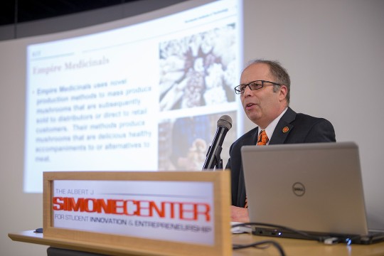 Man wearing glasses and suit talks at podium