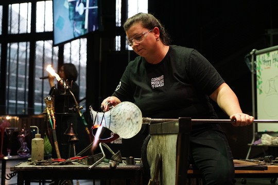 Woman fires glass pitcher in a hotshop.