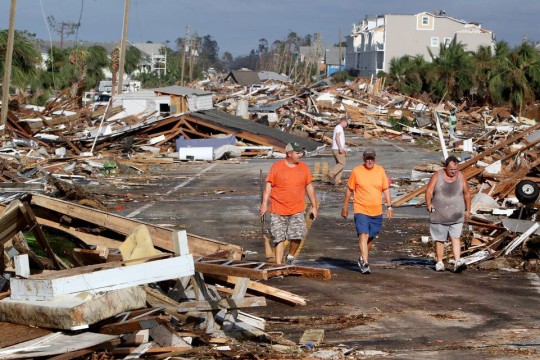 Three men walk through street strewn with debris from detroyed houses after a hurricane.