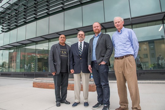 four men standing outside a glass building.