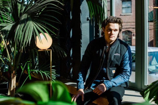 Sean Petterson sitting on a window sill surrounded by tropical plants.