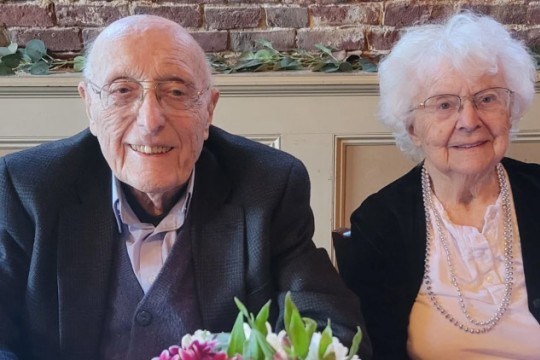 Richard Bicknell and his wife appear seated at a table with a bouquet of flowers in front of them