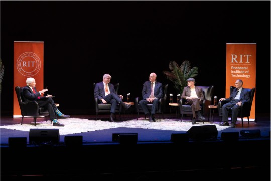 5 men sit on stage for an interview