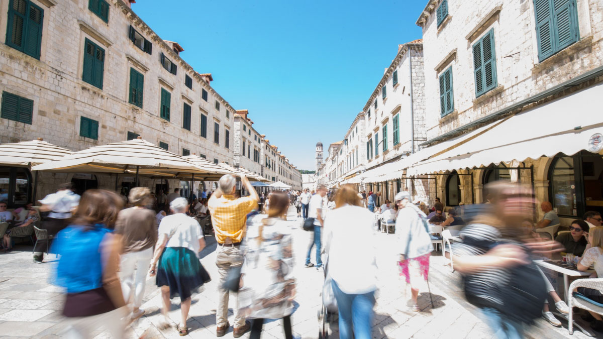 A bustling pedestrian street with people walking and sitting at outdoor cafes, lined with historic stone buildings.