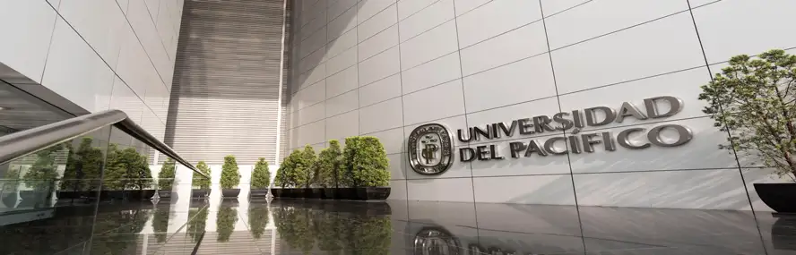 Modern university entrance with tall reflective walls, row of potted trees, and Universidad del Pacífico sign in metal letters.