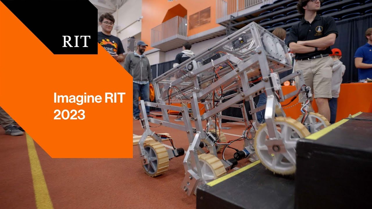 A robotic rover climbs steps at Imagine RIT 2023 while attendees observe and discuss the project.