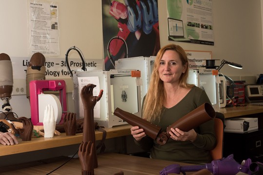 researcher holding a skin-colored 3D printed prosthetic arm. 