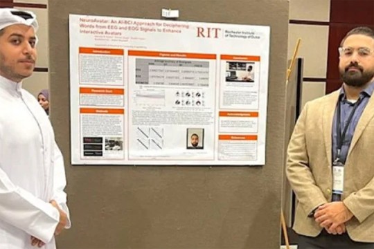 Two Emirati men stand on each side of a poster displaying their work at R I T Dubai.