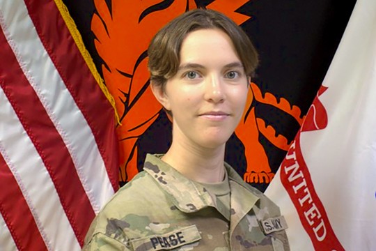 a woman with short brown hair sits in front of the american and R O T C flags