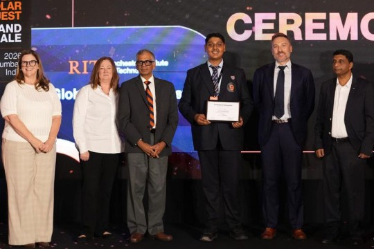 Student holds a certificate alongside officials and a tiger mascot at a Global Scholar Quest award ceremony.