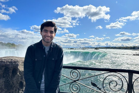a young man in a dark jacket stands at a fenceline near Niagara Falls.