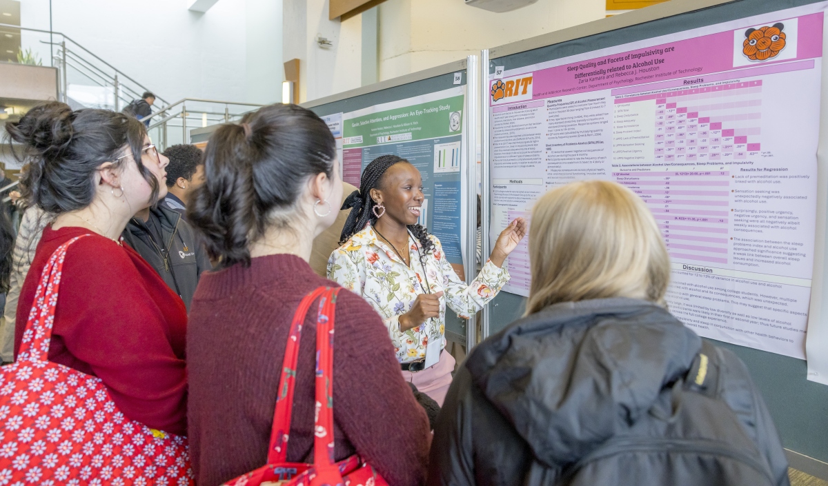 student presenting their poster to group of students during the 2025 graduate showcase in the fireside lounge, SAU