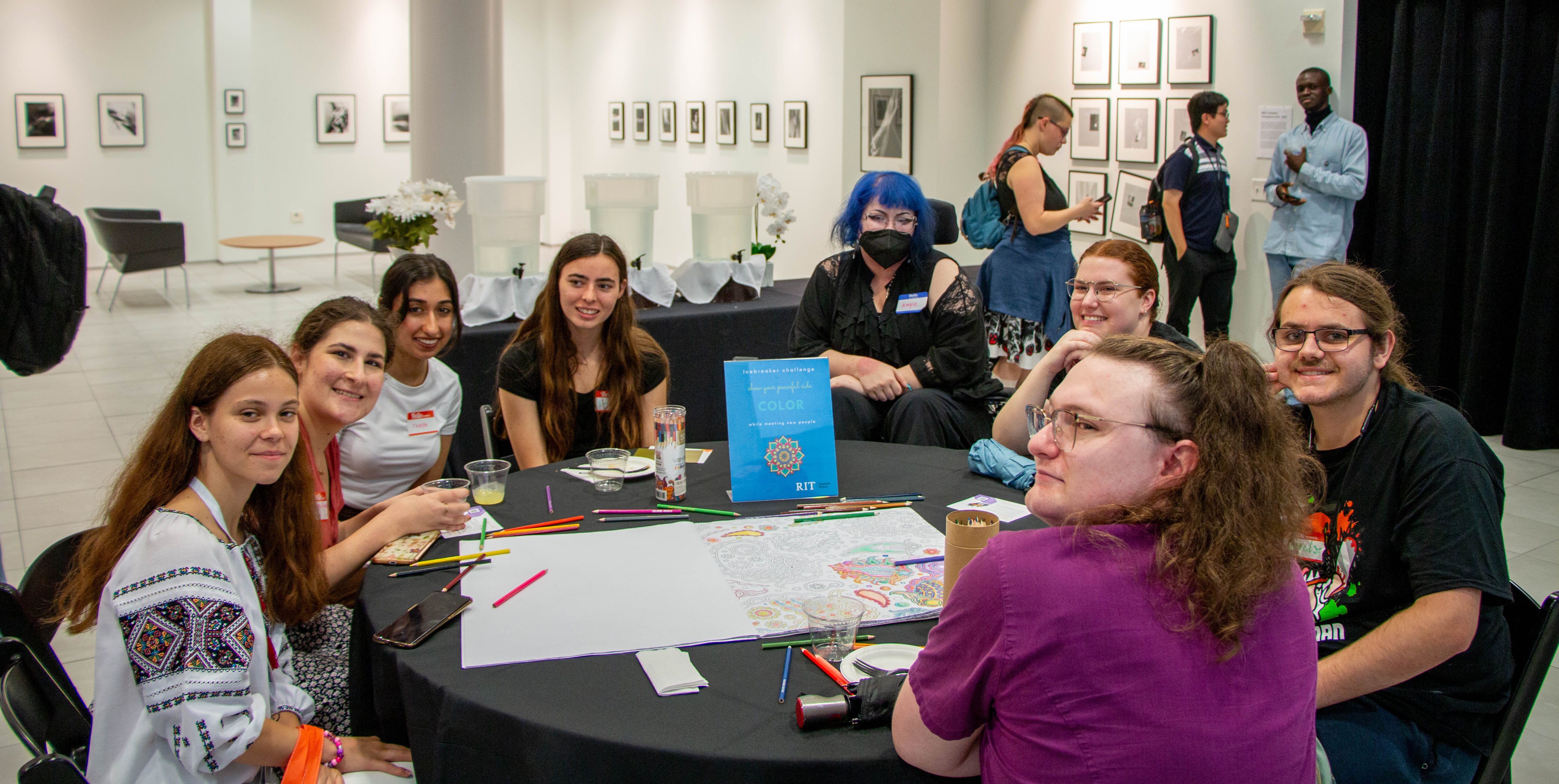 students sitting on a round table mingling and coloring a big coloring book