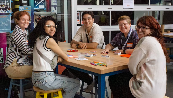 A group of smiling RIT graduate students pose together at Graduate Orientation  while playing ice breaker games