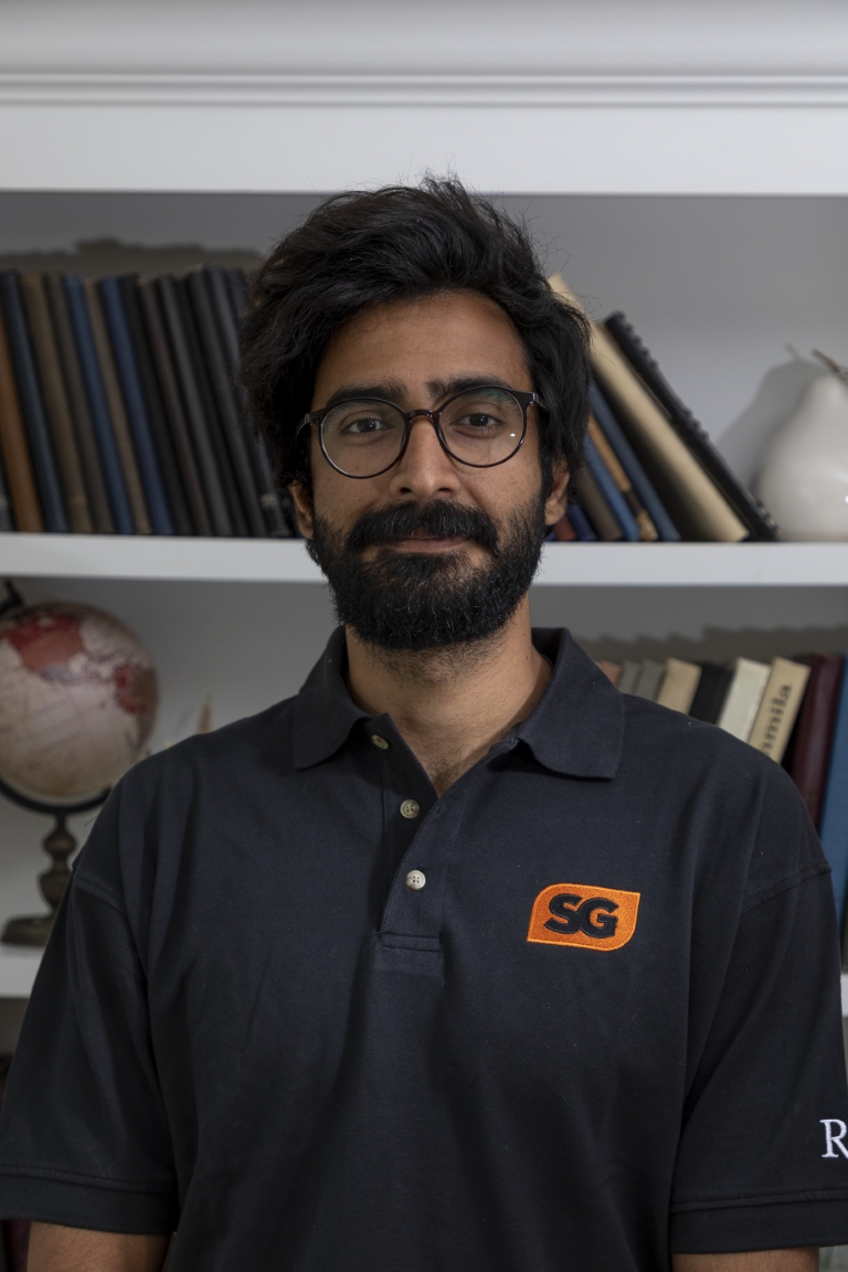 Shahzeb Jadoon in student government t-shirt with a bookshelf in the background