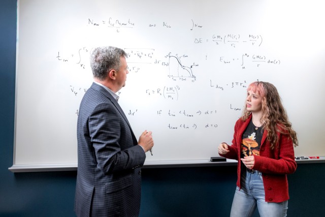 two people discuss a math problem written on a classroom board.