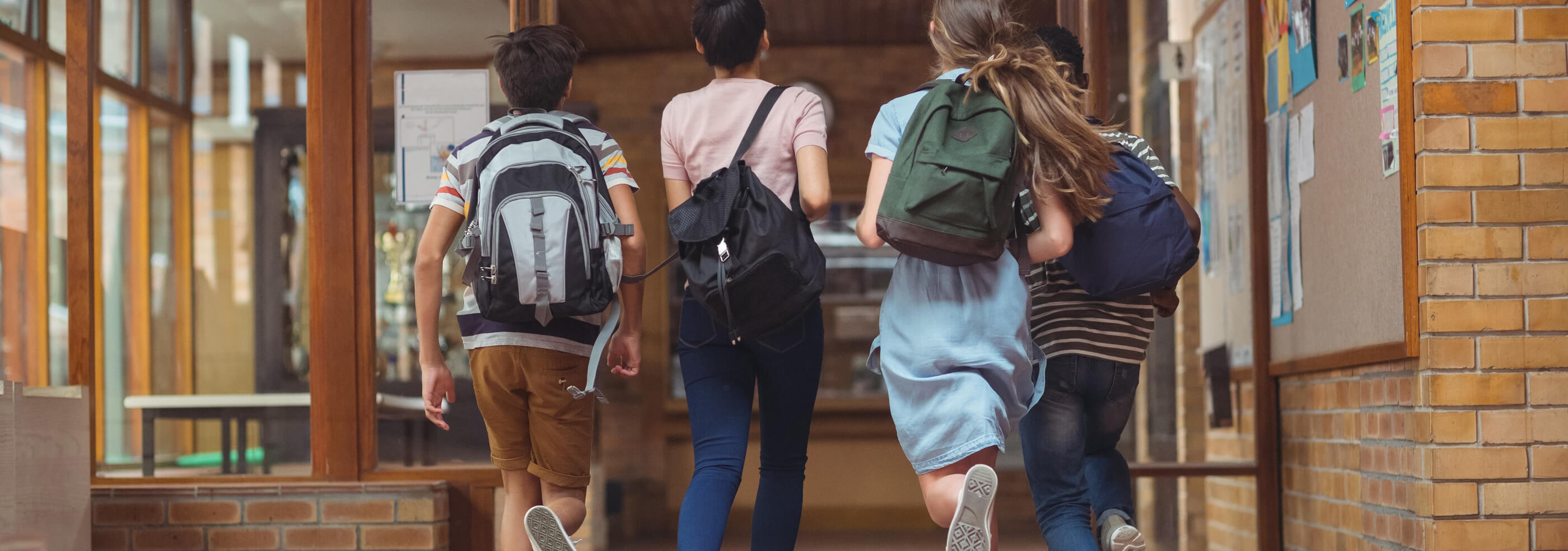 group of children running into school building with backpacks.