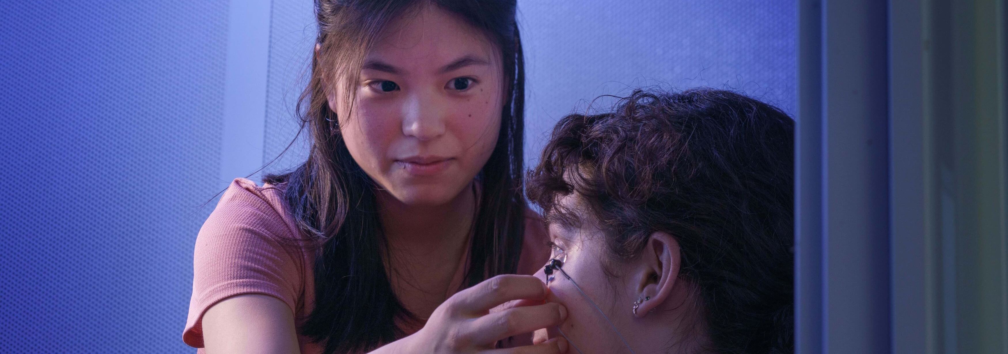 two lab members performing a research study, with one placing a sensor below the other's eye. Wires can be seen coming out of the sensor.