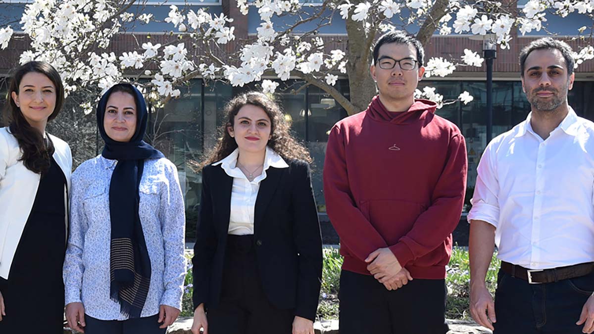 5 people standing outside, in front of a flowering tree.